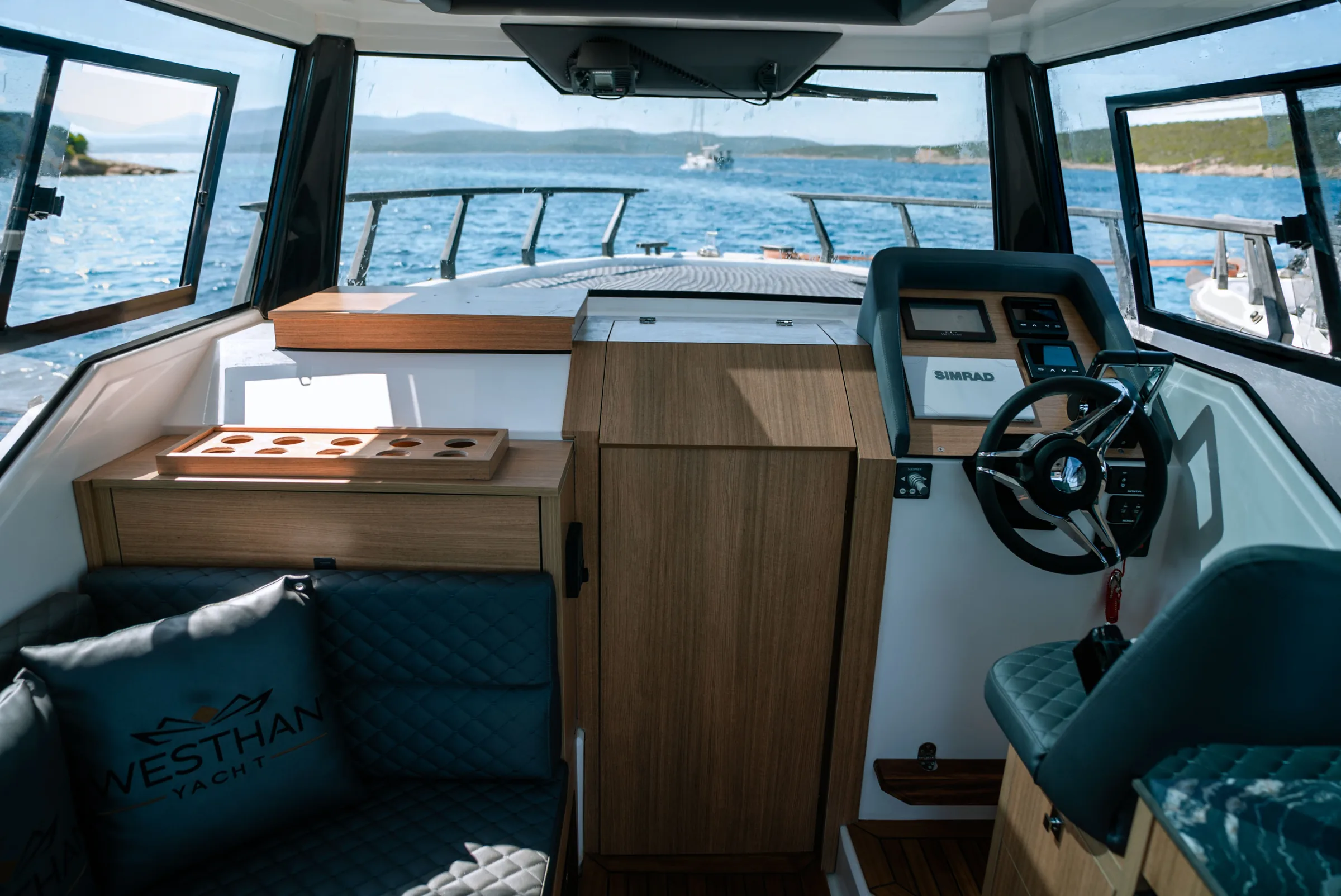 The helm: a wheel and a Simrad display beside a wood console, the windscreen and the sea ahead