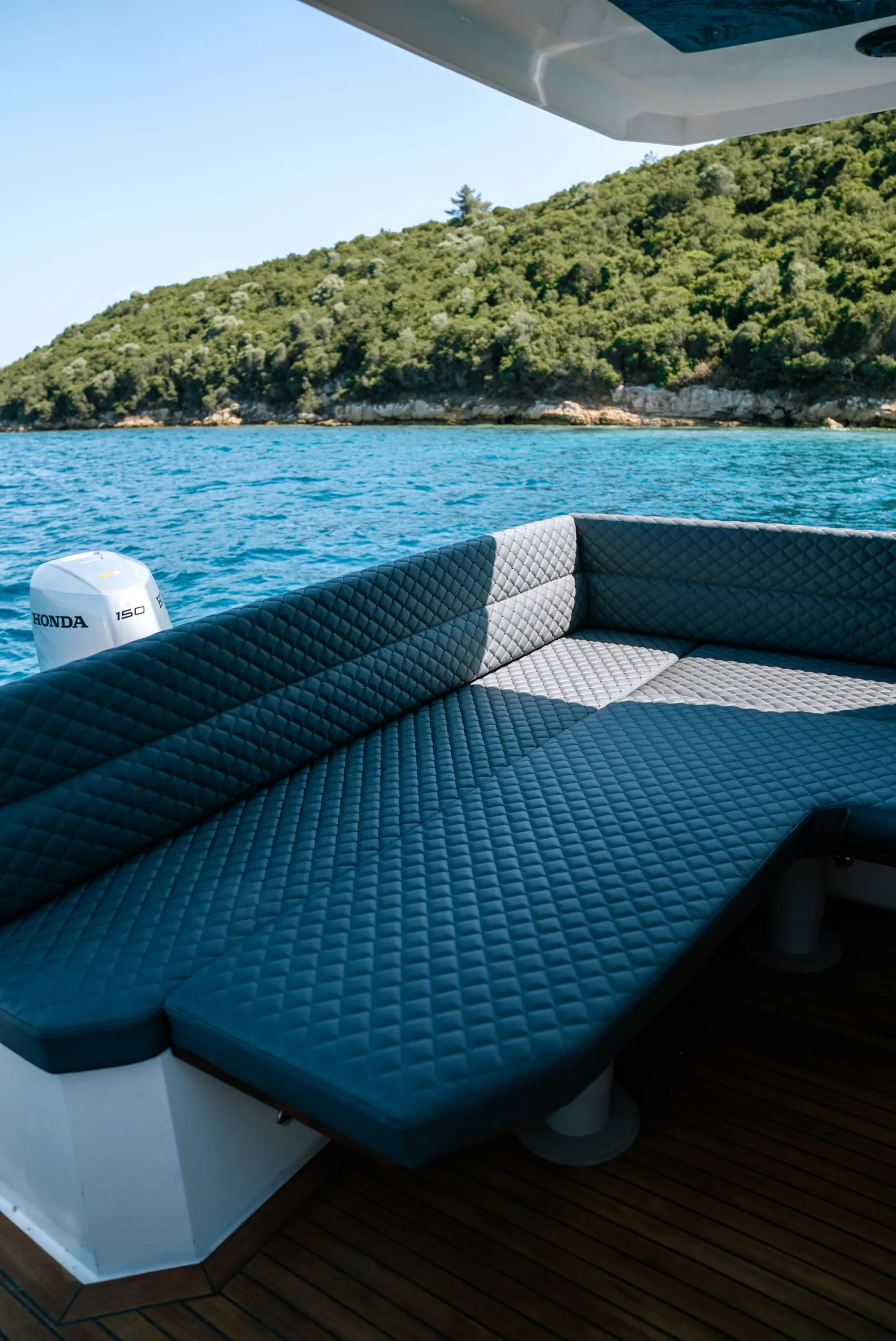 A wide quilted sunbed across the stern, an outboard and the shore behind it